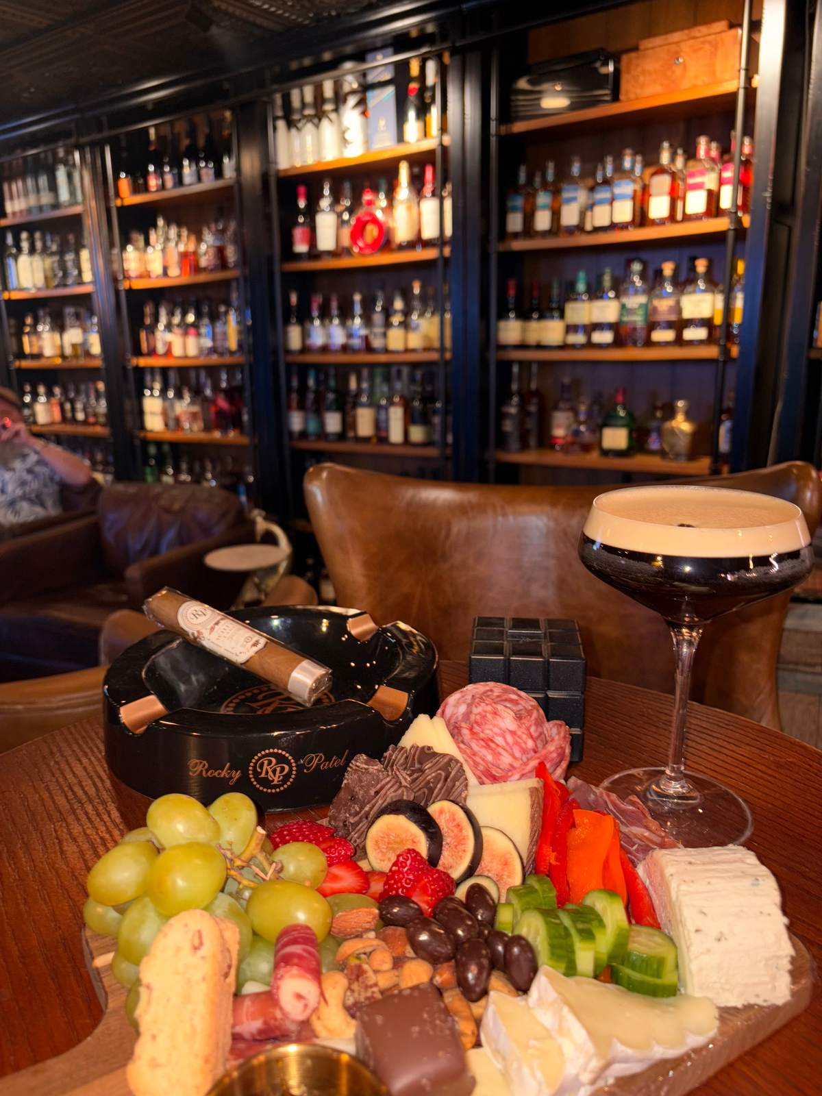 Charcuterie board and an espresso martini beside the spirits wall at Sun of a Gun Cigars & Spirits, Yuma, Arizona