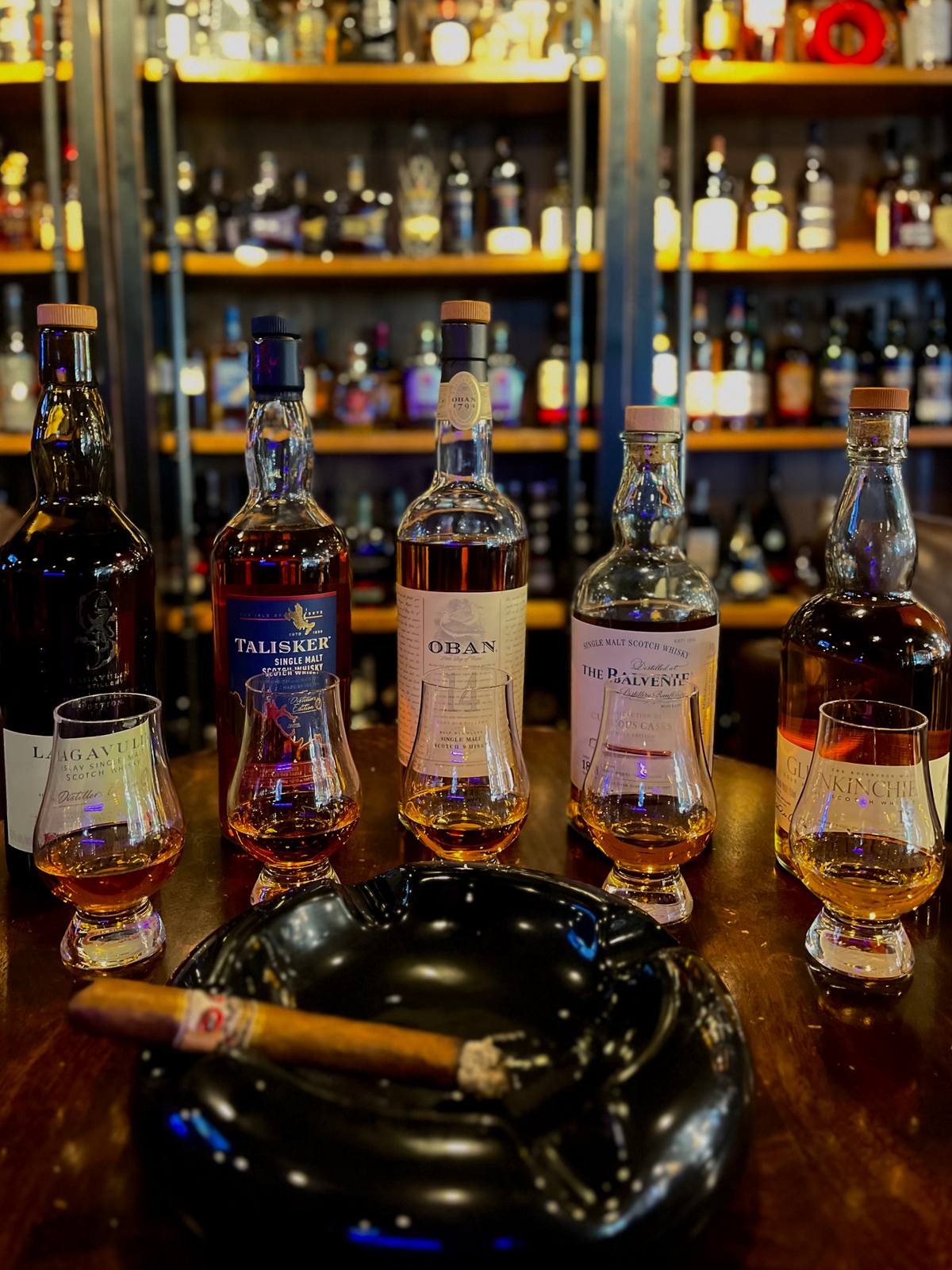 Single malt Scotch bottles, tasting glasses and a cigar in an ashtray at Sun of a Gun Cigars & Spirits, Yuma, Arizona